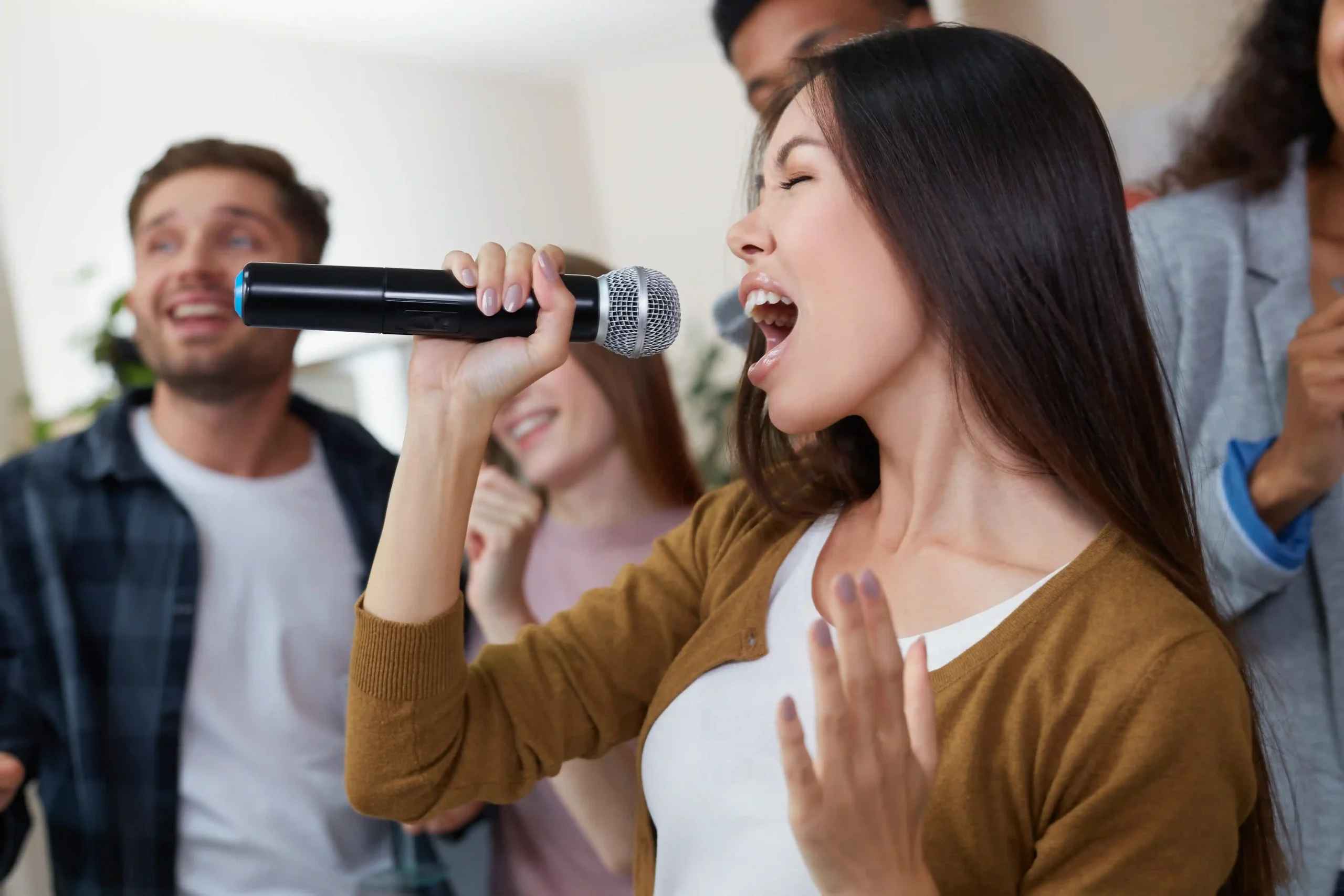Woman singing into a microphone with friends during karaoke, illustrating the social aspect of group singing lessons.